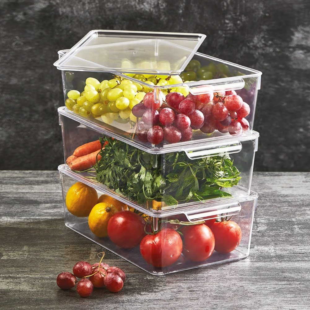 Contenedores transparentes apilados con frutas y verduras sobre fondo de madera.