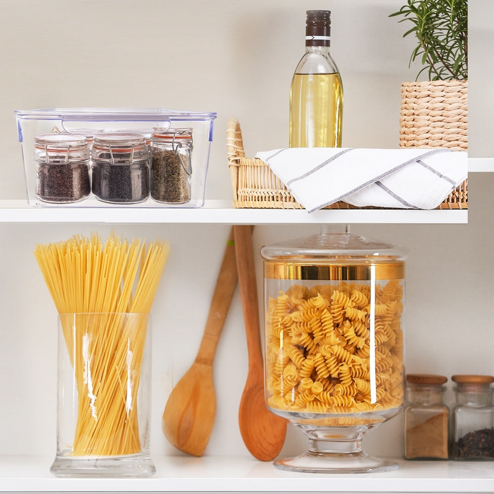 Frascos de especias, pasta, aceite y una maceta de hierbas en estantes.