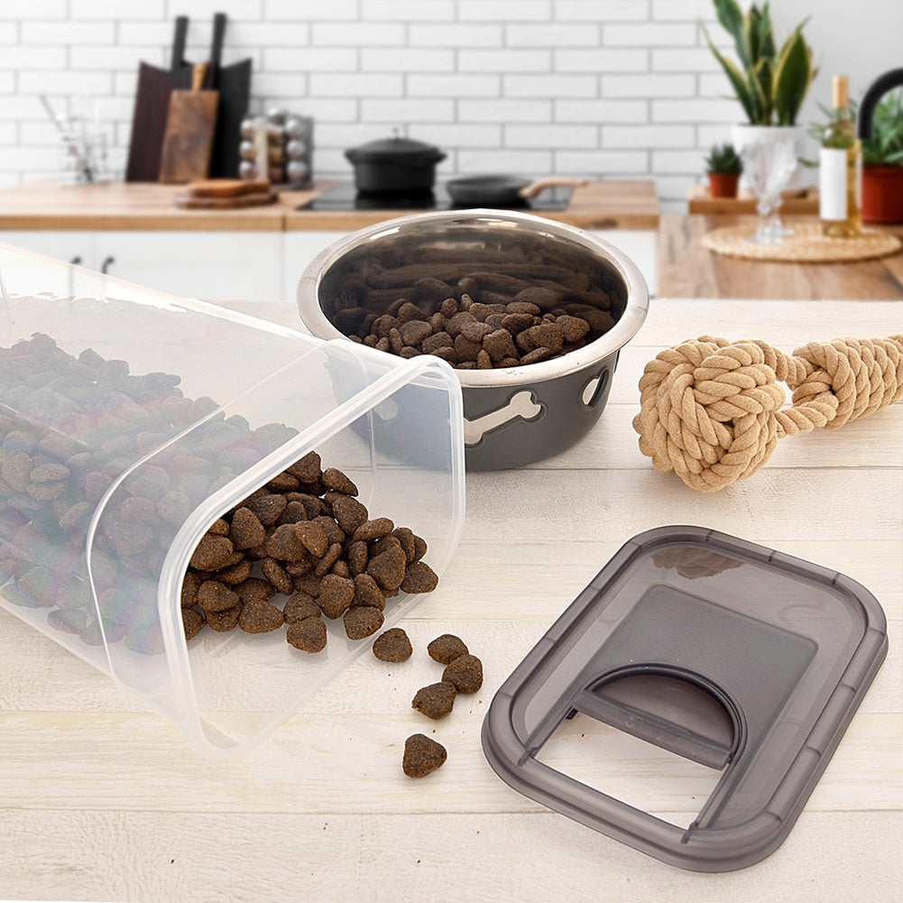 Un recipiente volcado con comida para perros, un cuenco, un juguete de cuerda y una tapa.