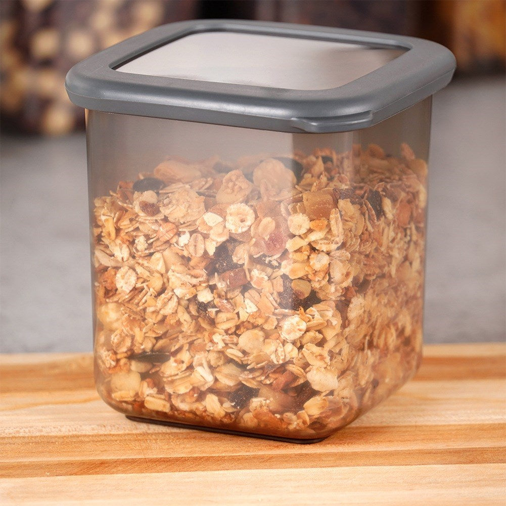 Un recipiente cuadrado transparente lleno de granola sobre una tabla de cortar de madera.