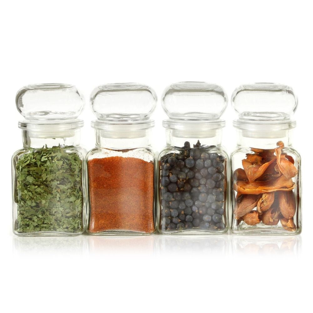 Cuatro frascos de vidrio con especias: hierbas, pimentón, bayas de enebro, nuez.