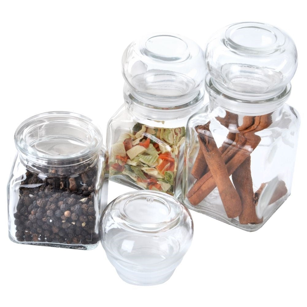 Cuatro frascos de vidrio con especias: granos de pimienta, verduras secas y canela.