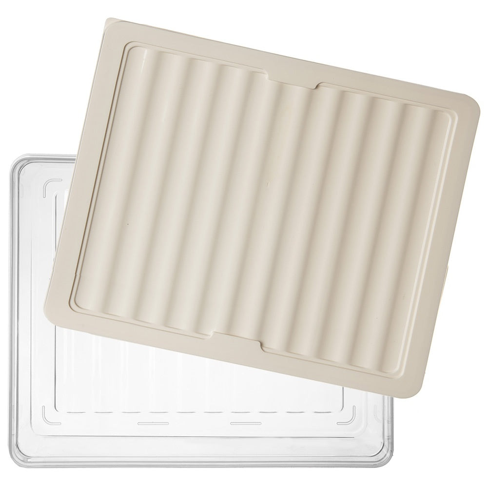 Una tapa de plástico beige acanalada descansa sobre una caja de plástico transparente.