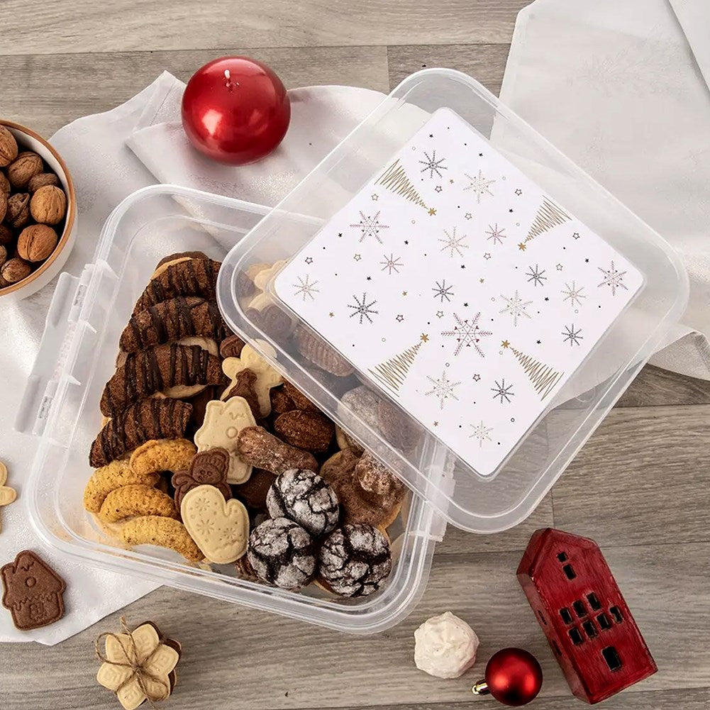Galletas navideñas en un recipiente transparente, con nueces, vela roja y casa cerca.