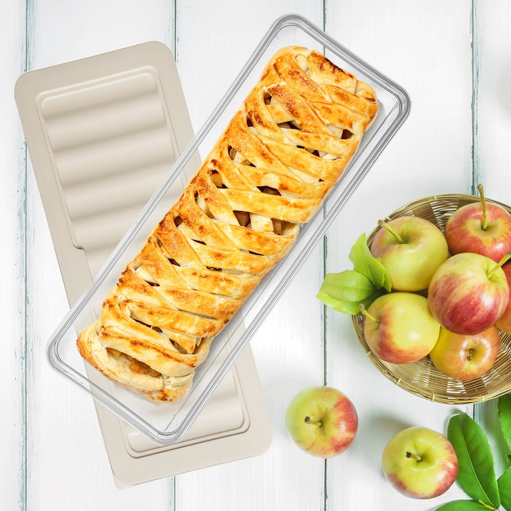 Un strudel de manzana dorado y marrón en un plato de vidrio junto a una cesta de manzanas.