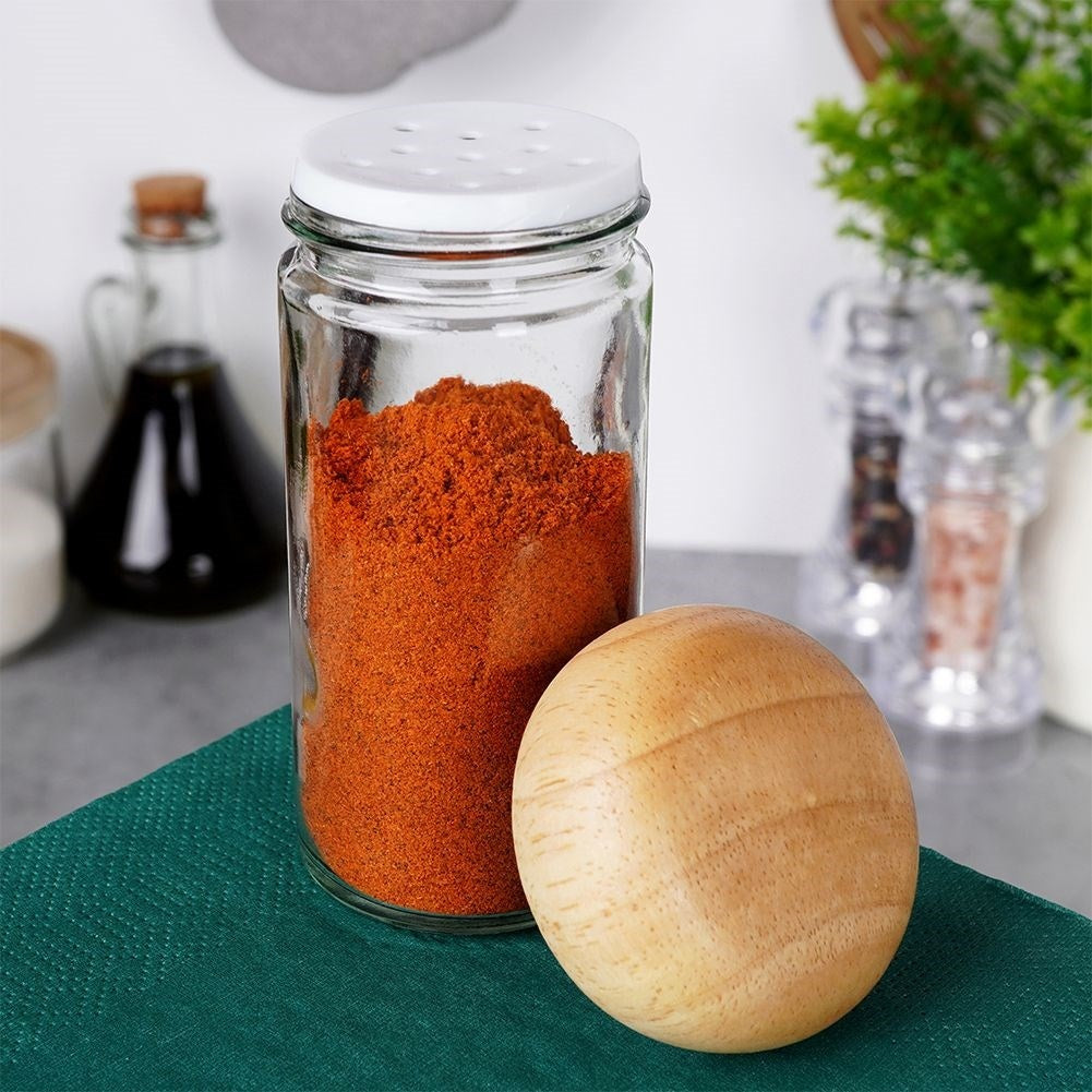 Un frasco de vidrio con polvo rojo y una bola de madera al lado sobre un paño verde.