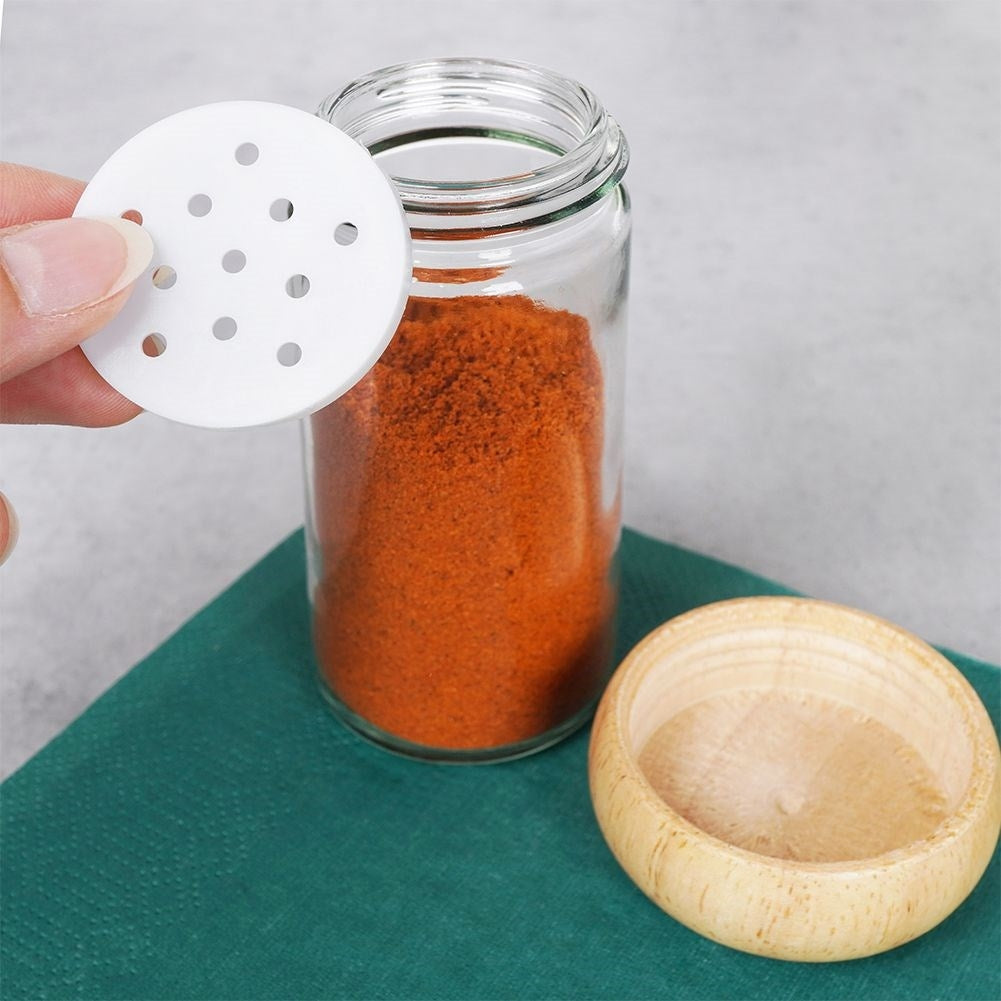 Un frasco de vidrio con polvo rojo, un tapa de madera y una tapa perforada blanca.