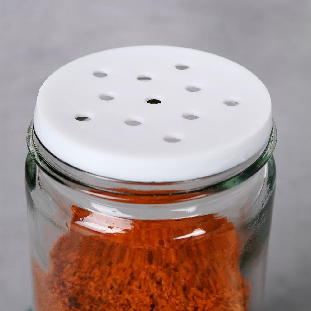Un frasco de vidrio con tapa blanca, lleno de especias. Varios agujeros.
