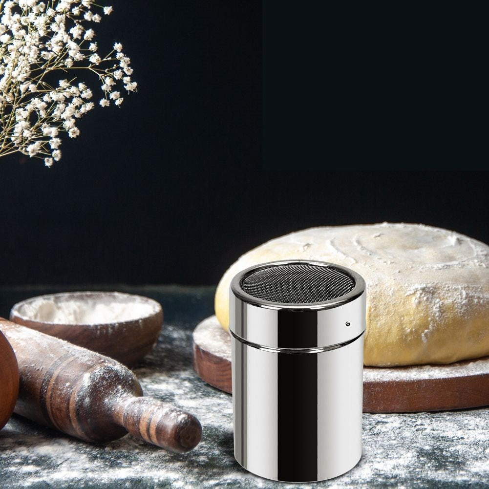 Un colador de acero inoxidable junto a un pan y un cuenco de madera con harina.