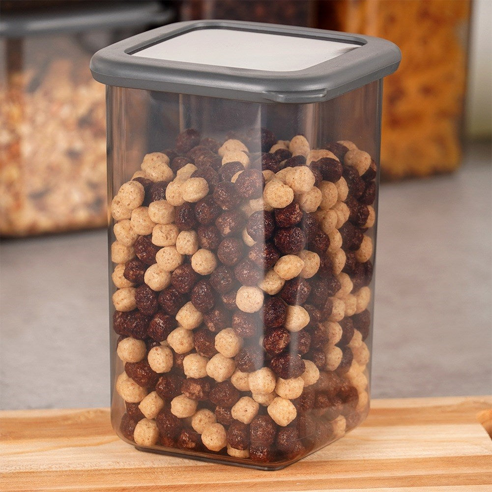 Un recipiente rectangular de plástico transparente con tapa gris, lleno de cereales marrones y claros.