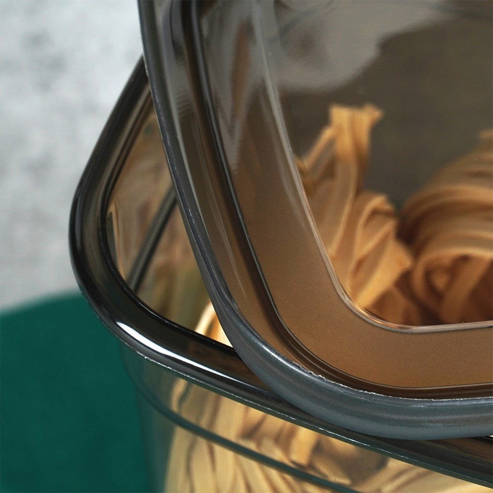 Primer plano de un recipiente transparente con pasta, cuya tapa oscura está parcialmente abierta.