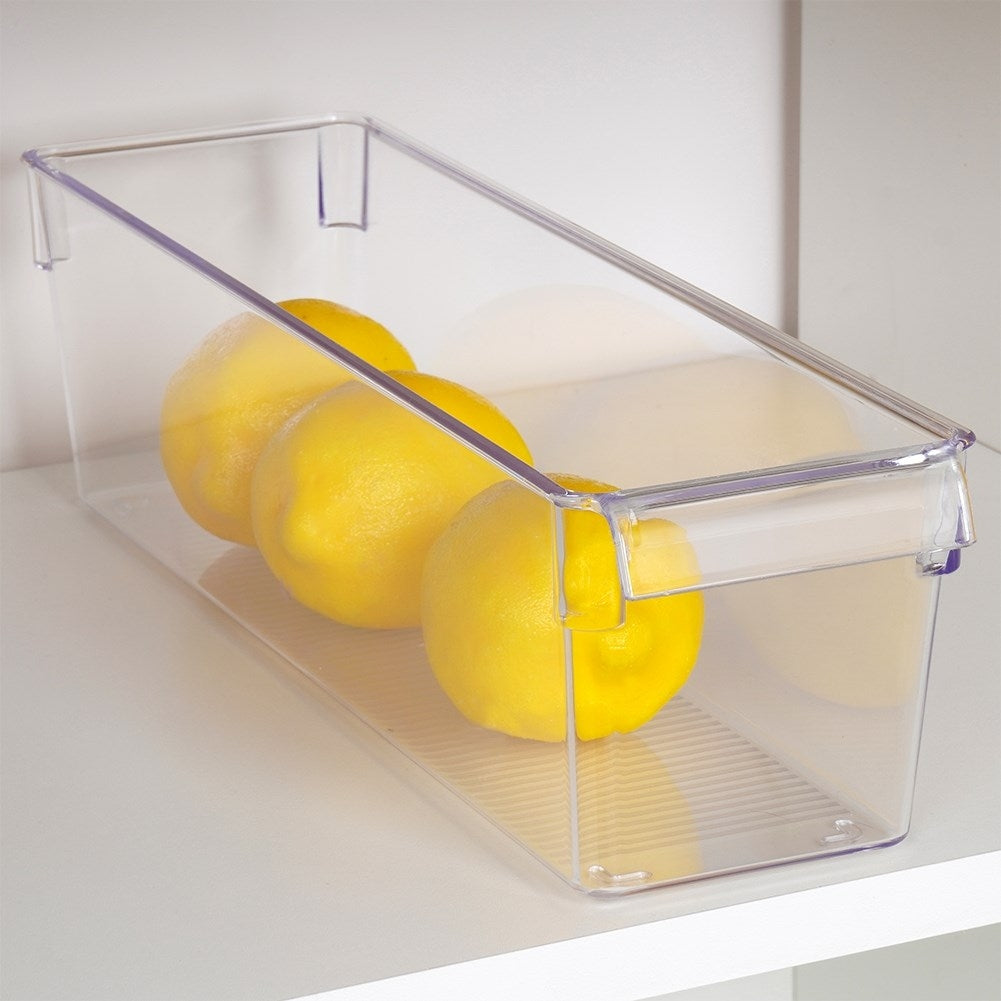 Tres limones amarillos dentro de un recipiente transparente en un estante blanco.