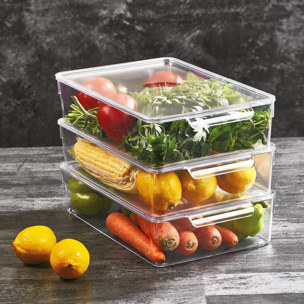 Contenedores transparentes apilados con frutas y verduras frescas como tomates, hierbas, maíz, limones y zanahorias.