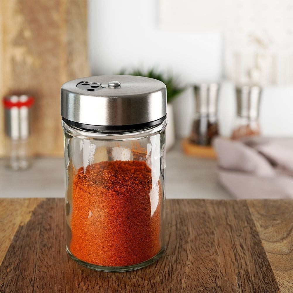 Un frasco de vidrio con especia roja y tapa metálica sobre superficie de madera.