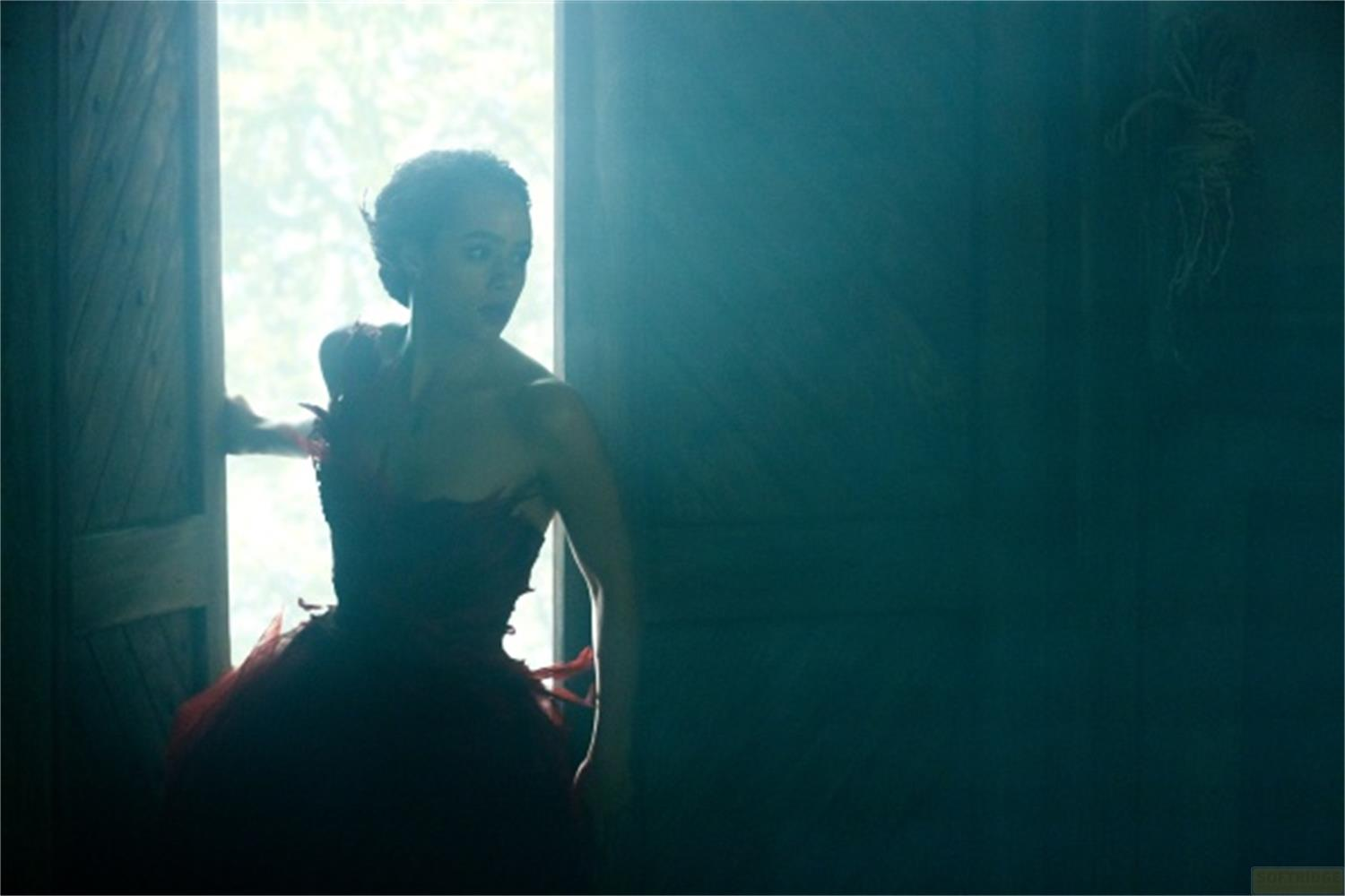 Donna in abito rosso in un vano porta, guarda indietro.