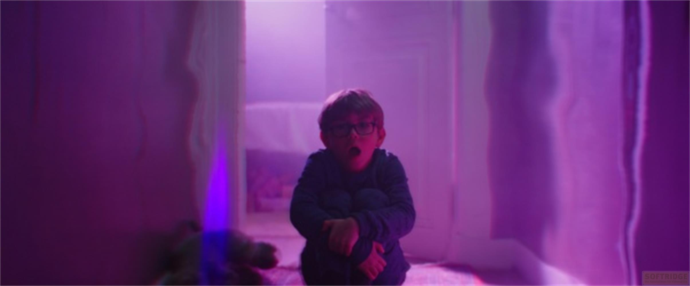 Un ragazzo con gli occhiali seduto a terra in una stanza illuminata di viola.