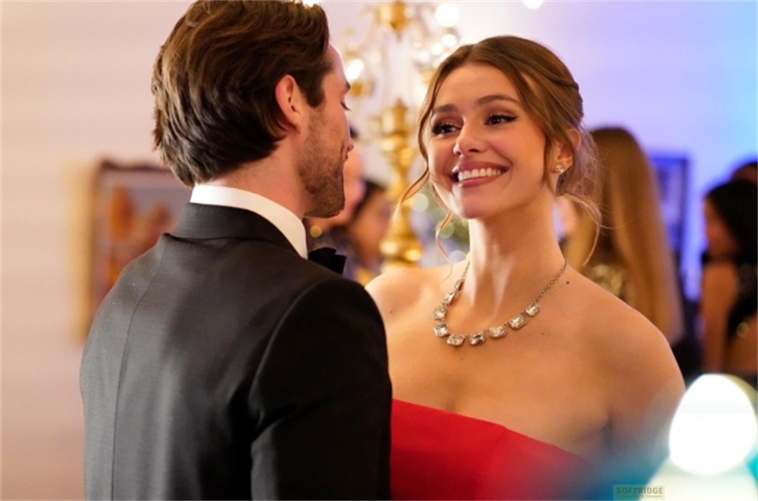 Un uomo in abito nero e una donna in rosso si sorridono.