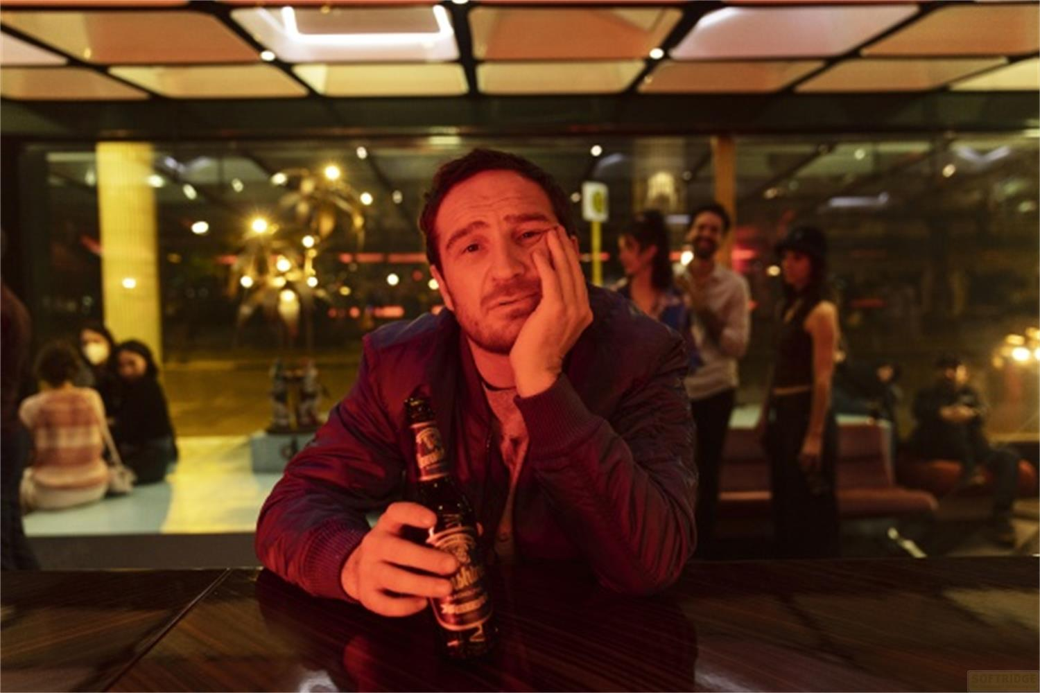 Un uomo è seduto al bar con una bottiglia di birra, appoggiando il mento sulla mano.