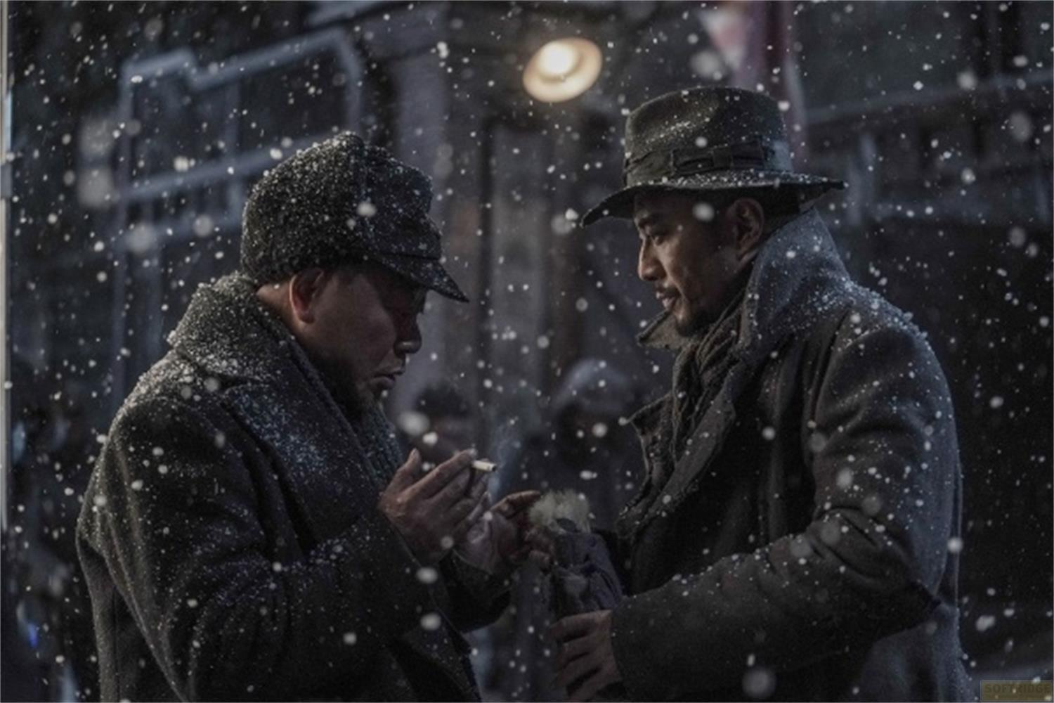Due uomini con cappelli e cappotti stanno nella neve che cade, uno accende una sigaretta.