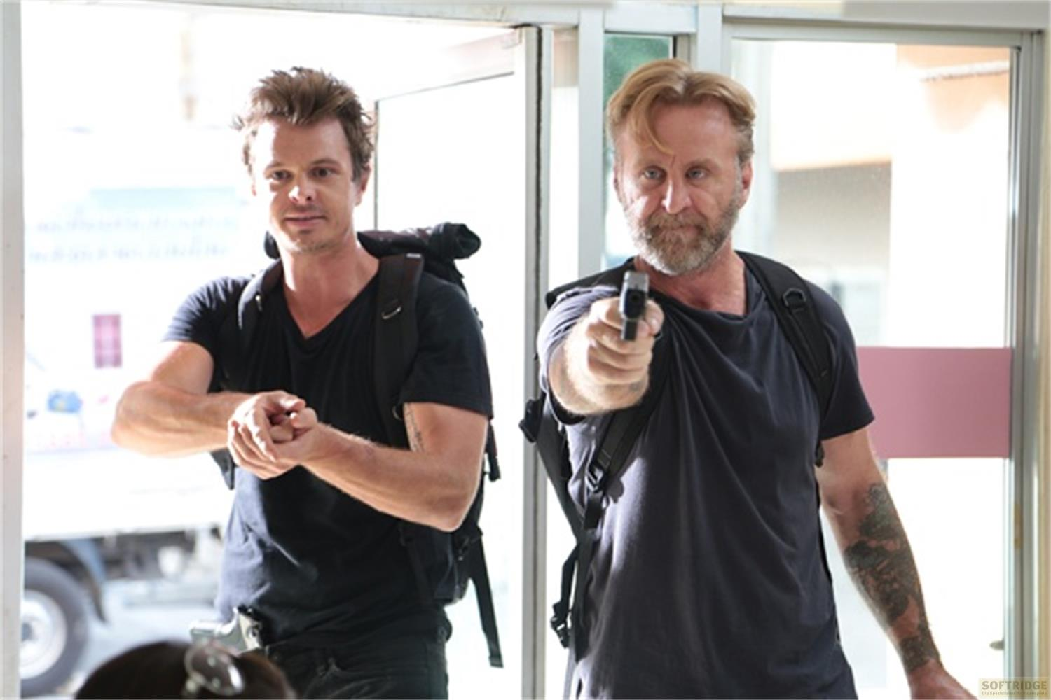Deux hommes avec des sacs à dos. L'un vise avec un pistolet.