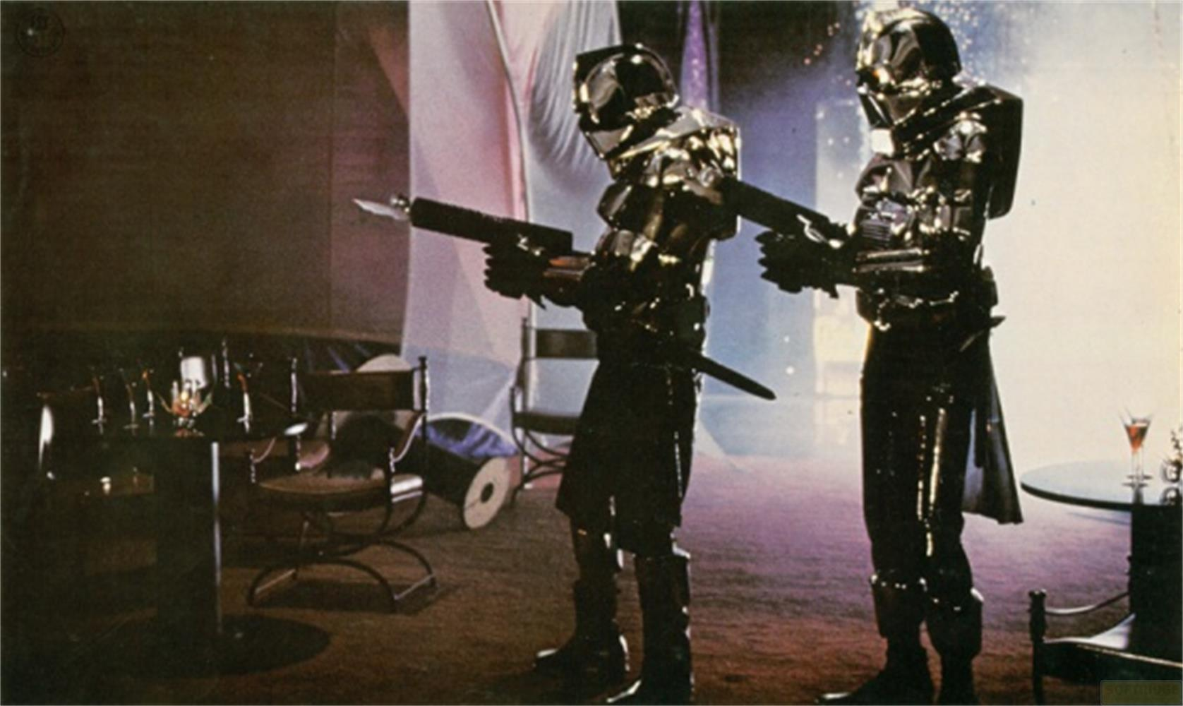 Due figure in armatura futuristica con armi si trovano in una stanza con mobili.