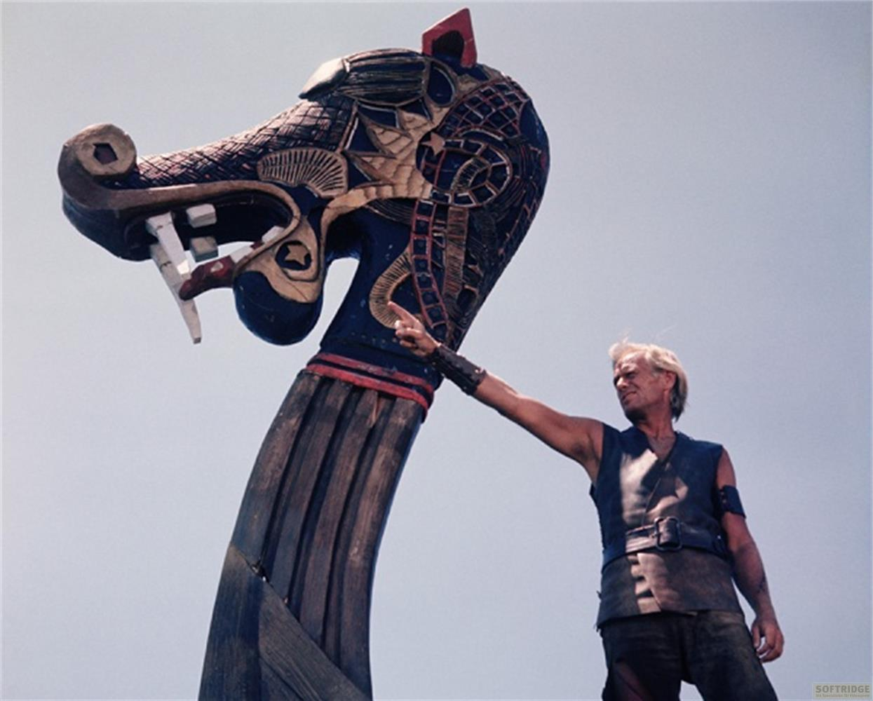 Uomo tocca scultura testa di drago nave vichinga contro cielo.