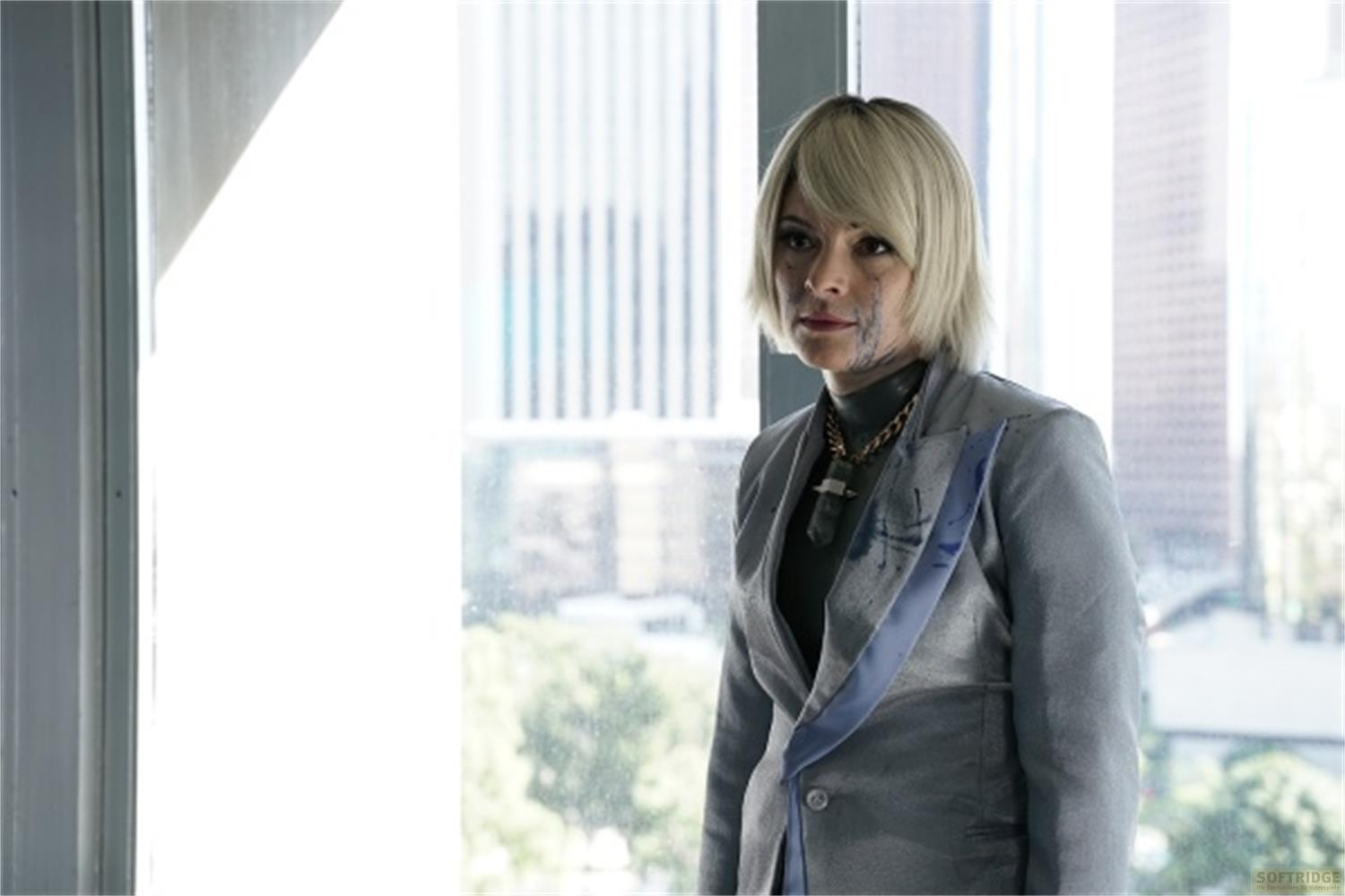 Una donna con capelli biondi e vernice blu sul viso indossa un tailleur grigio.