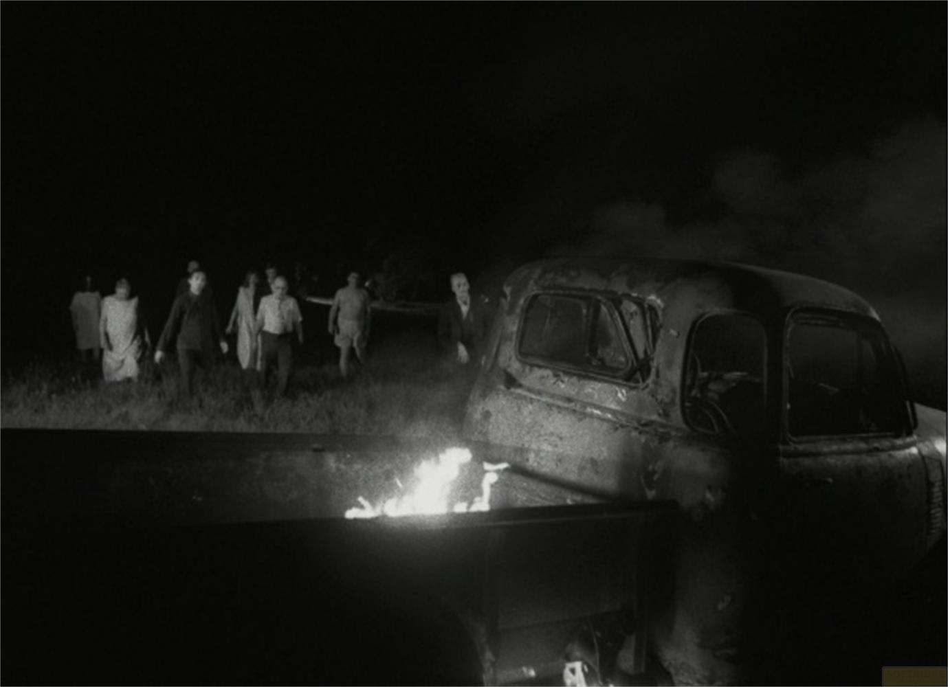 Un gruppo di persone si avvicina a un camion in fiamme di notte.