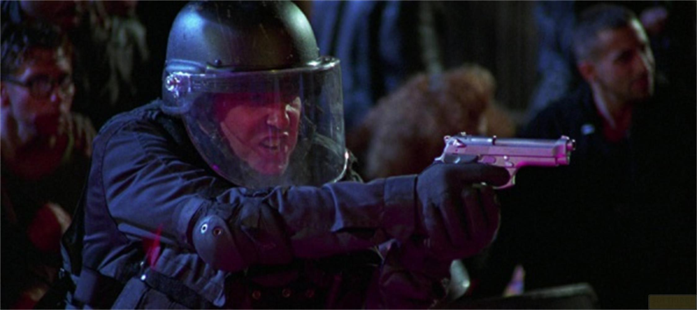Un uomo in equipaggiamento protettivo, casco e visiera tiene una pistola d'argento.