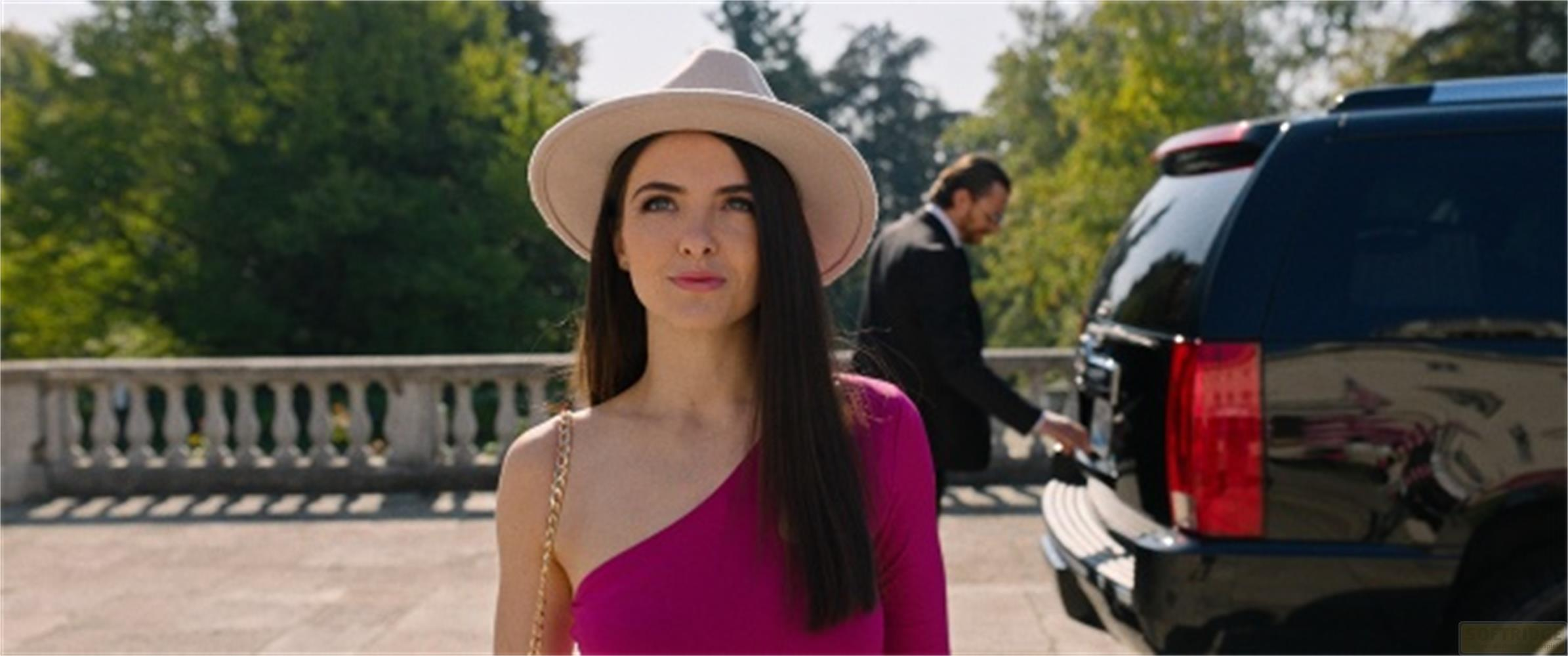 Donna in abito rosa e cappello vicino a SUV nero, uomo in abito sullo sfondo.
