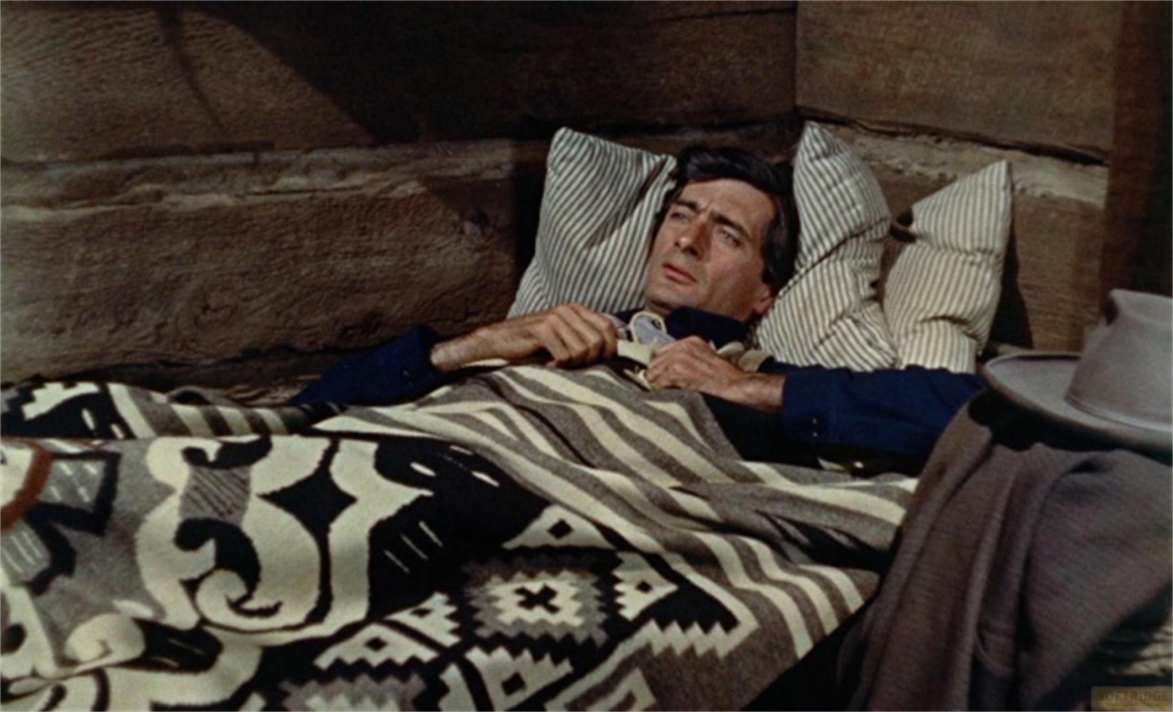 Un uomo giace a letto, coperto da una coperta fantasia.