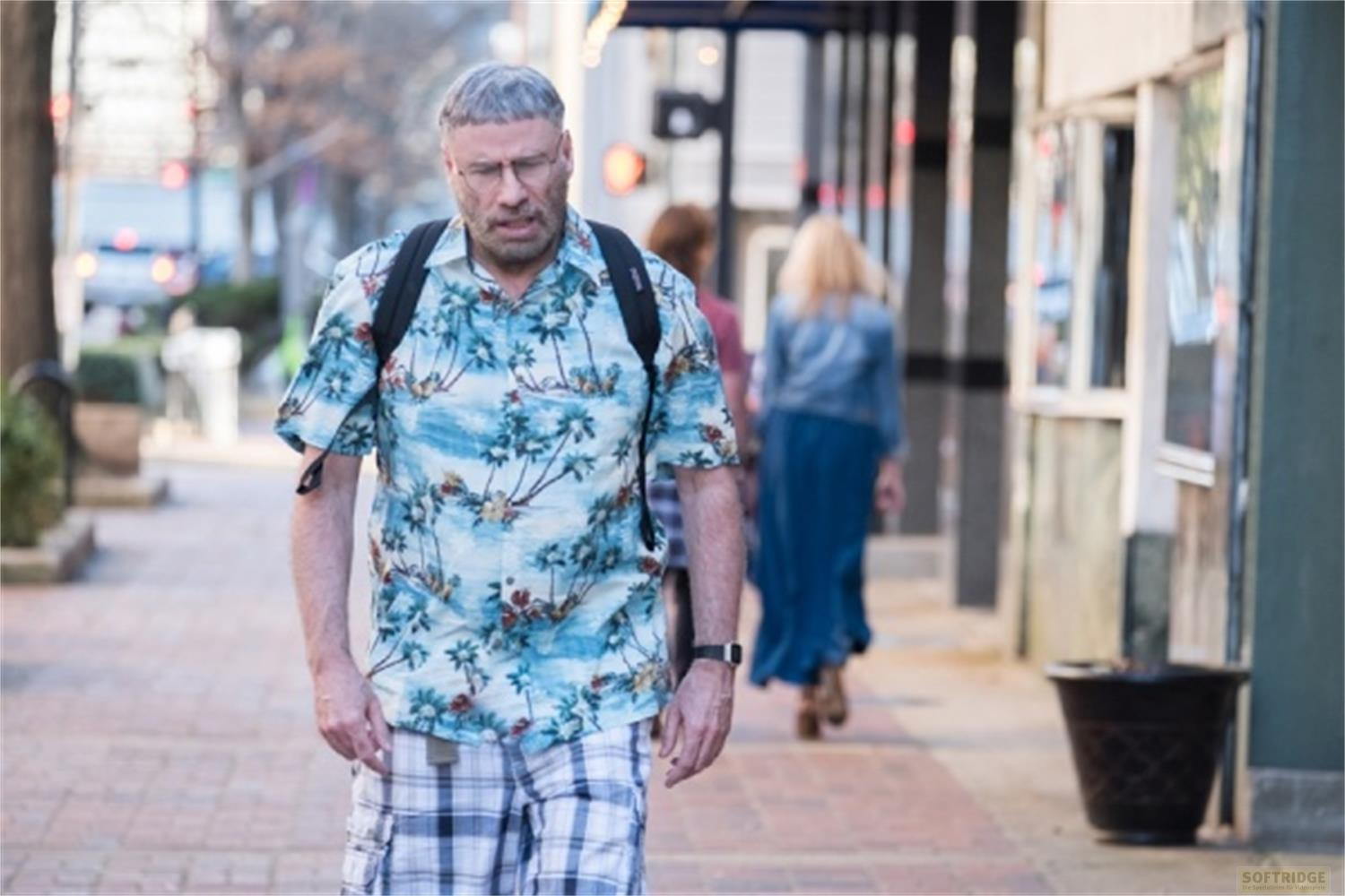 Un uomo con occhiali e camicia hawaiana cammina su un marciapiede.