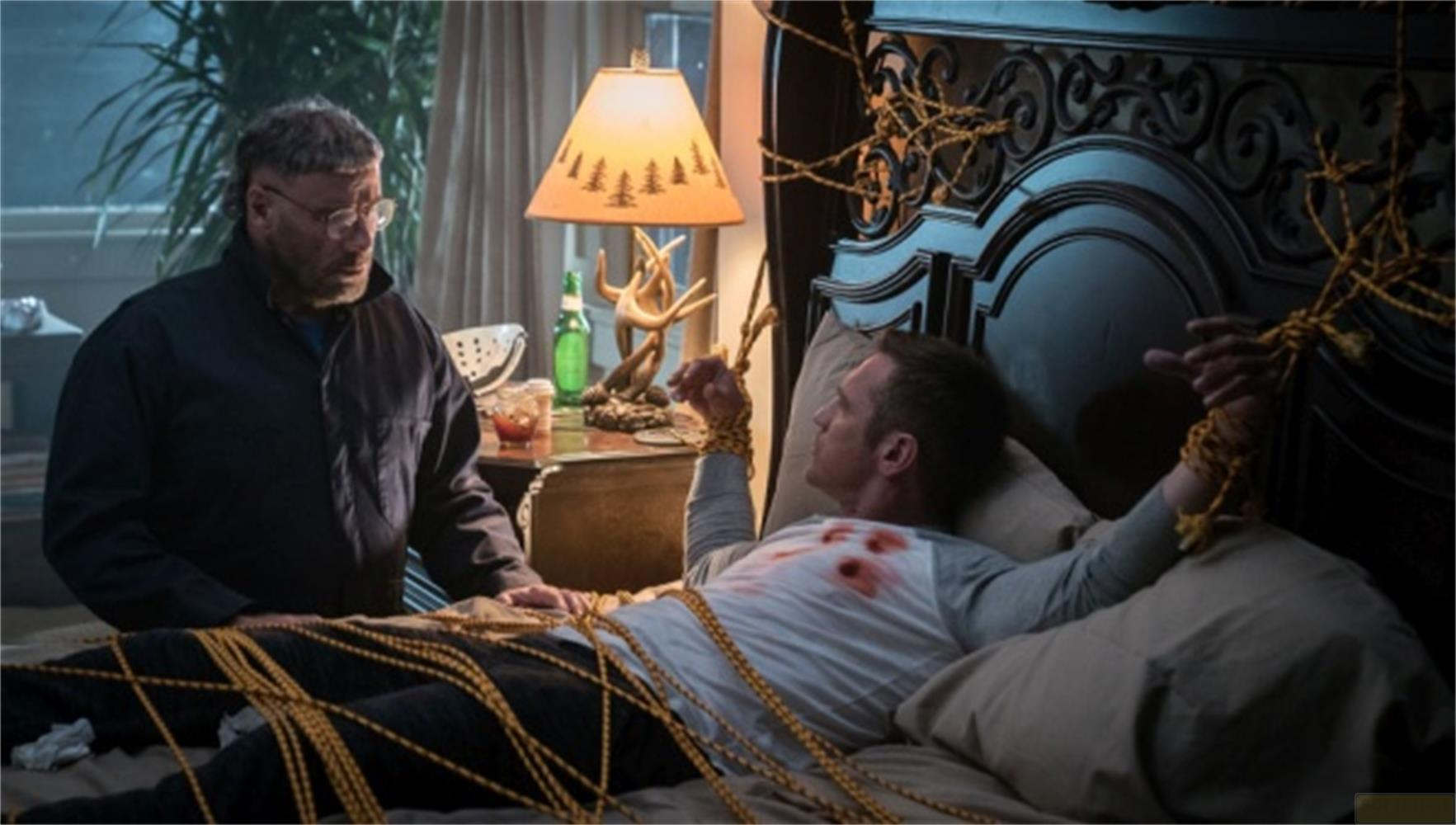 Un uomo giace legato a letto, un altro uomo sta accanto a lui.