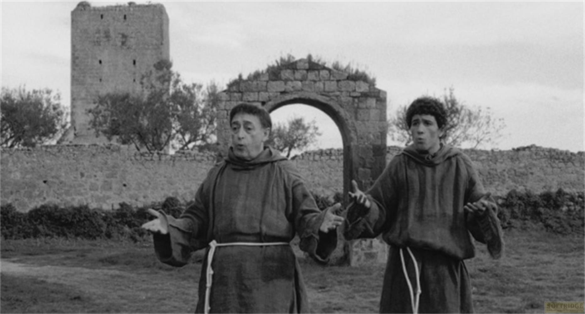 Due monaci in tonaca stanno davanti a un vecchio muro di pietra e un arco.