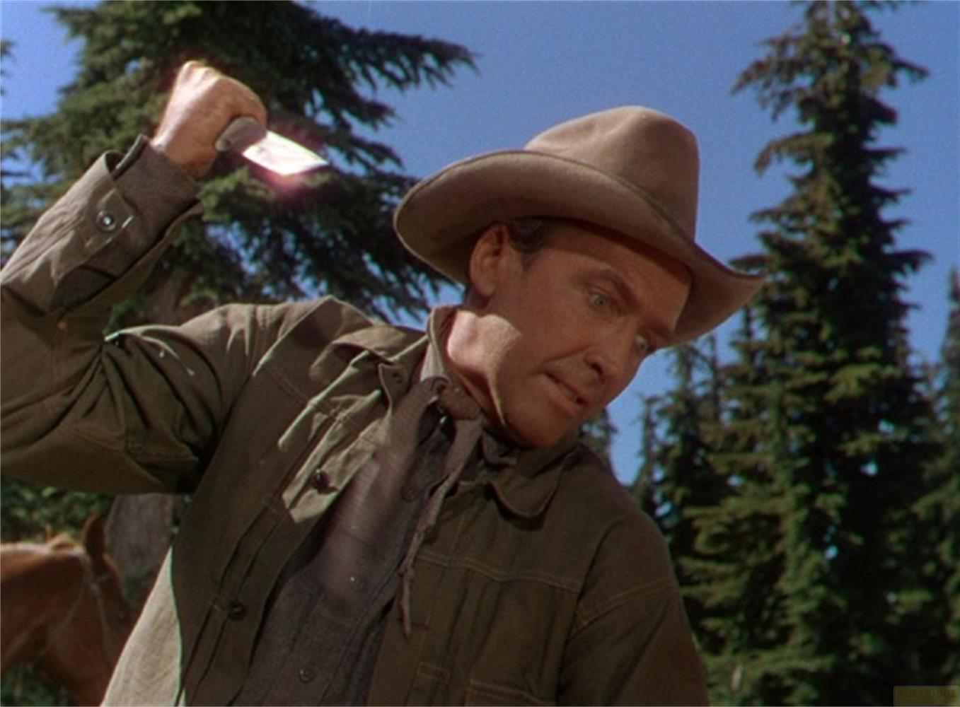 Un uomo con cappello tiene un coltello in un bosco.