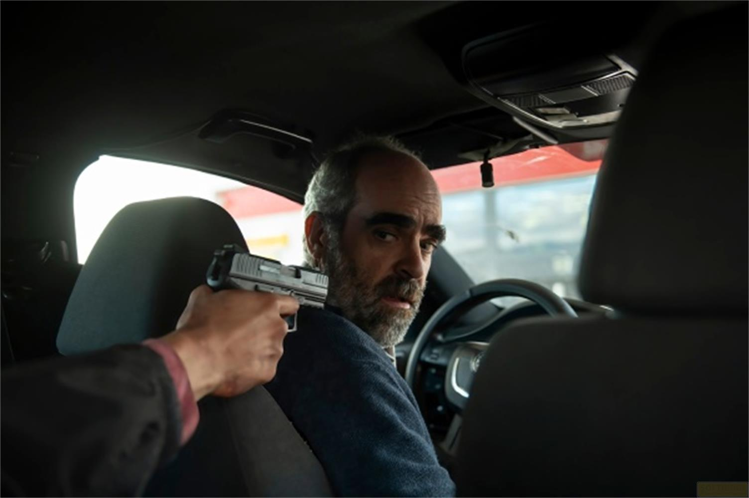 Un uomo viene minacciato con una pistola da dietro in un'auto.