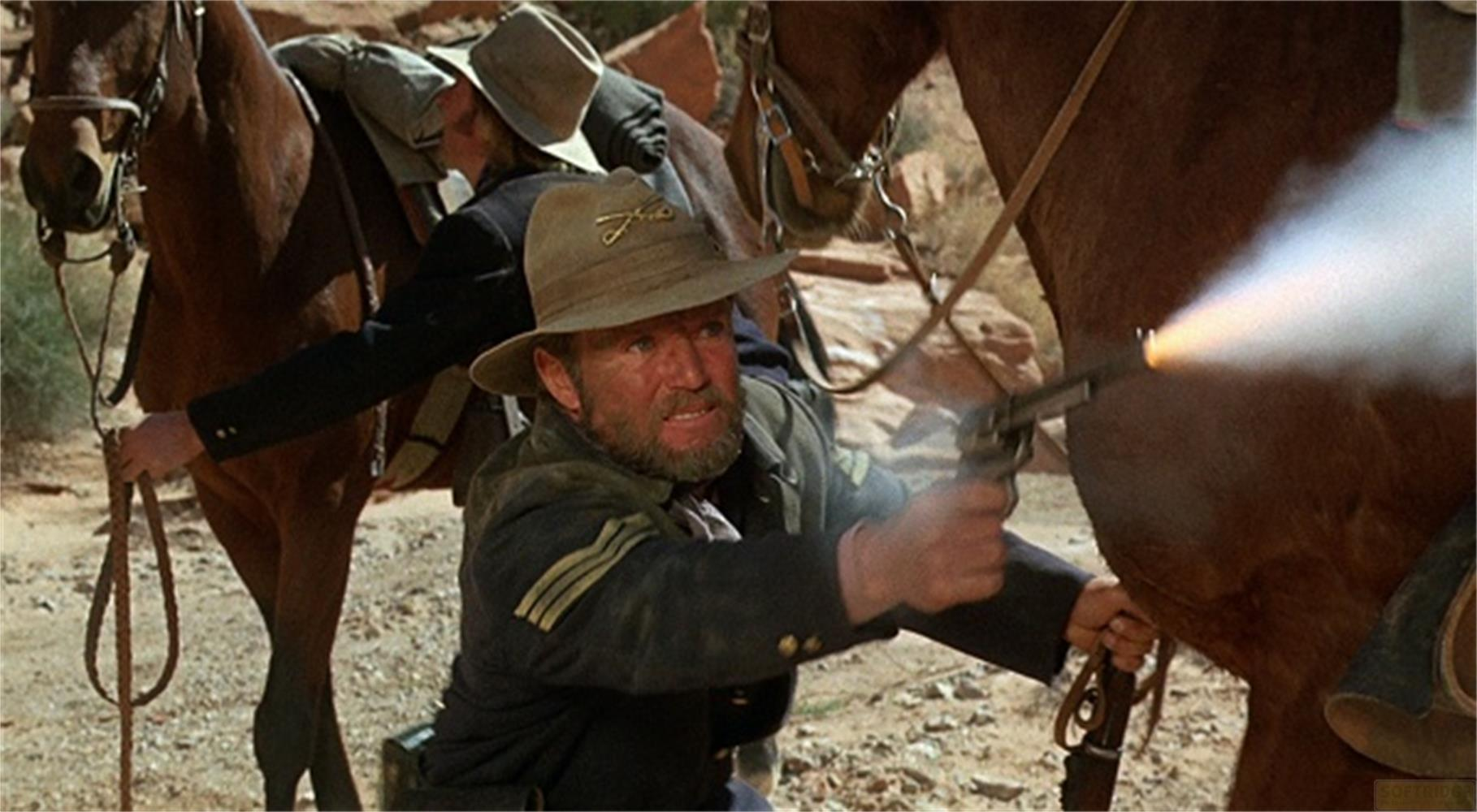 Uomo in divisa spara revolver, fumo sale, davanti a cavallo.