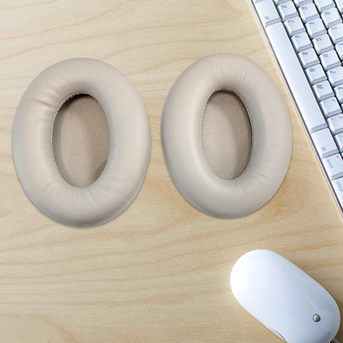 Dwie kremowe poduszki na uszy leżą obok siebie na drewnianym biurku obok klawiatury i myszy.