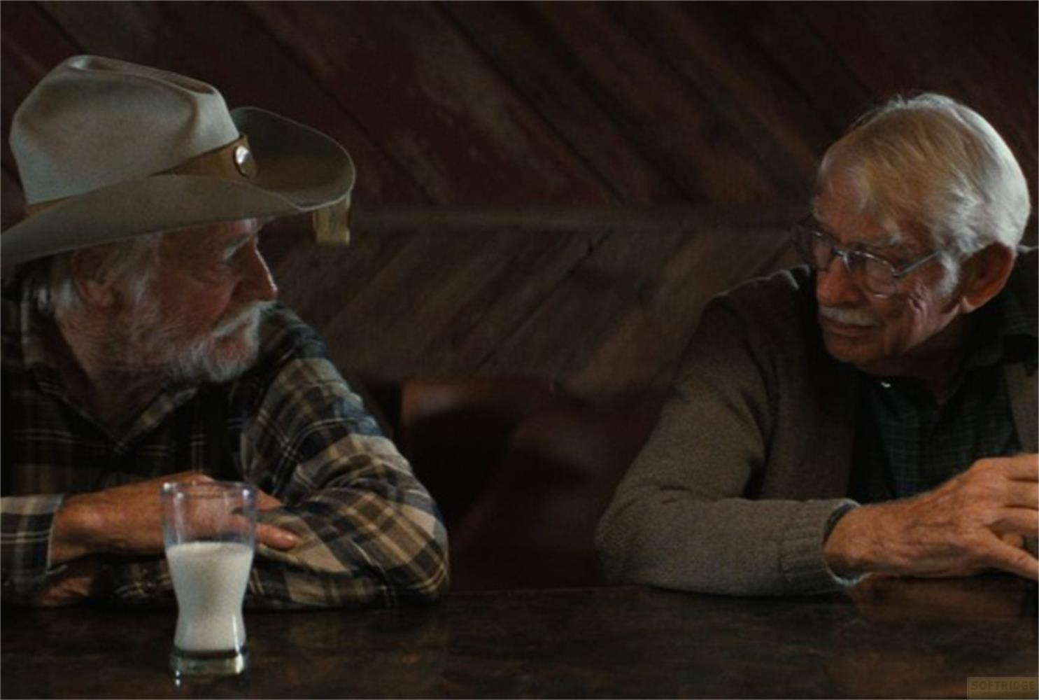 Due anziani seduti a un tavolo. Uno indossa un cappello da cowboy e una camicia a quadri.
