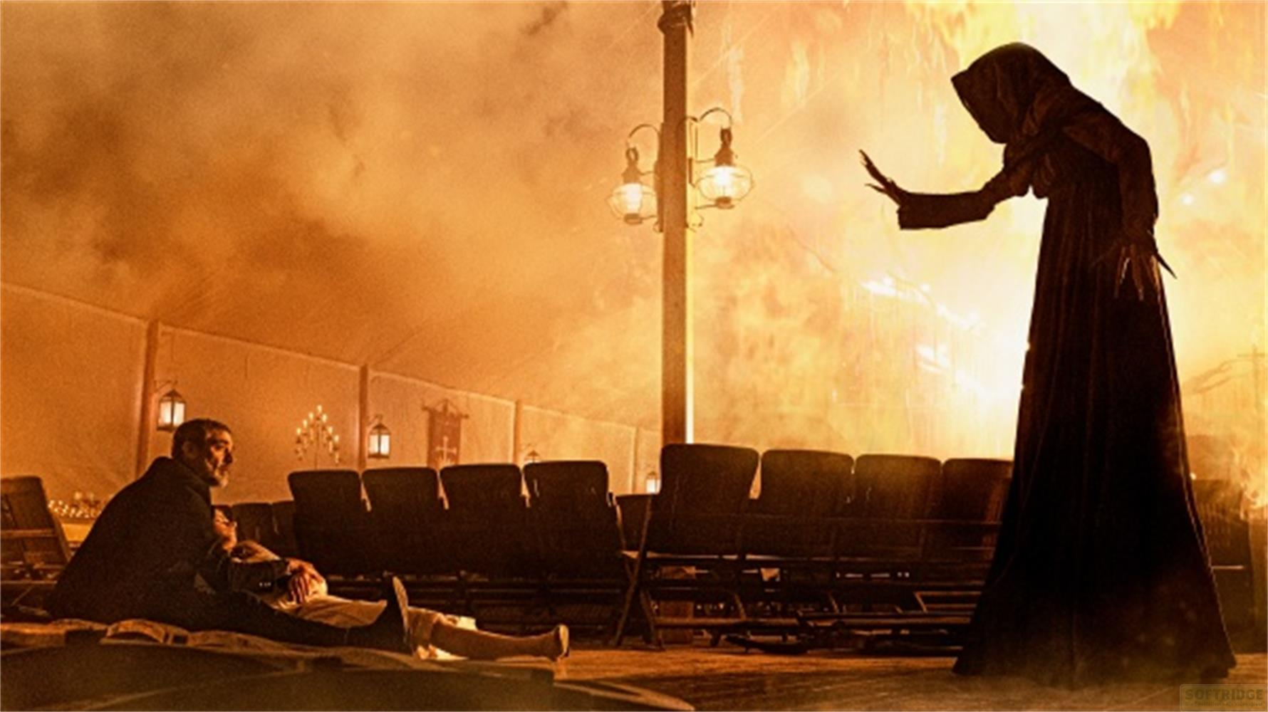 Una figura incappucciata davanti alle fiamme; due persone sedute davanti.