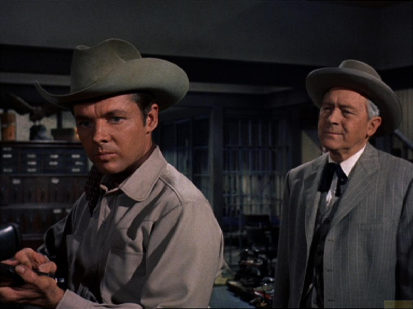 Due uomini con cappelli da cowboy stanno in una stanza. Uno indossa un gilet, l'altro un abito.