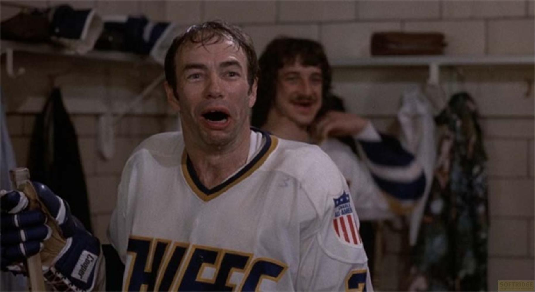 Un joueur de hockey bouche bée, regardant la caméra. Un autre homme se tient derrière lui.