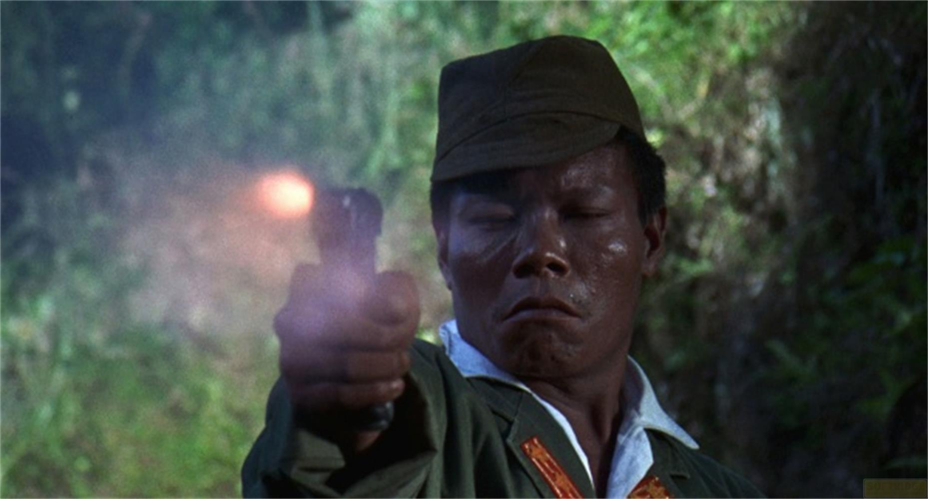 Un uomo dalla pelle scura con un berretto spara con una pistola, fumo visibile.