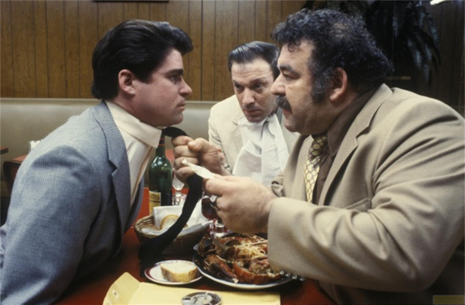 Uomo afferra cravatta di un altro; un terzo guarda. Cena con aragosta.