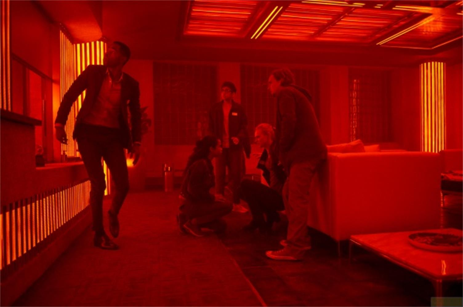 Cinque persone in una stanza illuminata di rosso con mobili.