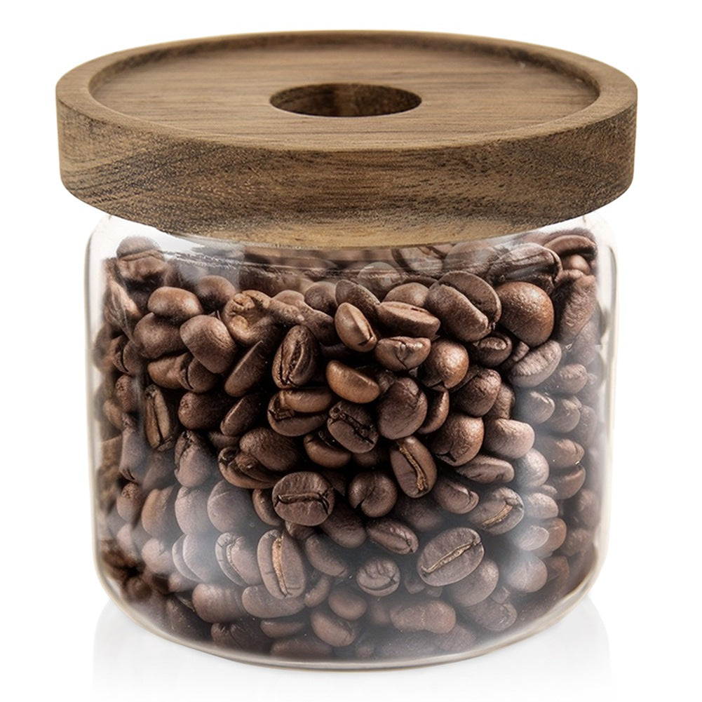 Frasco de vidrio lleno de granos de café, con tapa de madera y agujero.