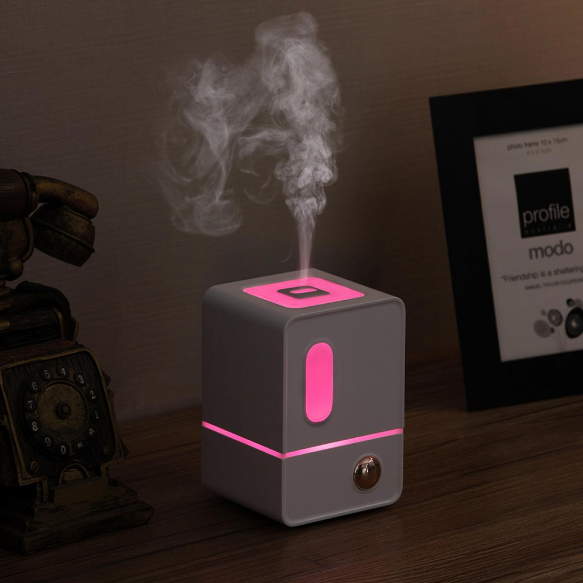 Grauer Diffusor mit rosa Lichtern gibt Dampf ab. Daneben ein altes Telefon und ein Bilderrahmen.