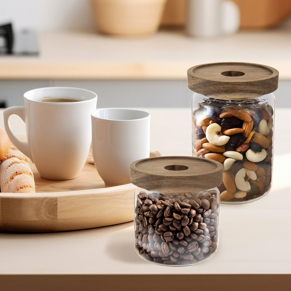 Dos tazas blancas y dos frascos con nueces y granos de café en una mesa.