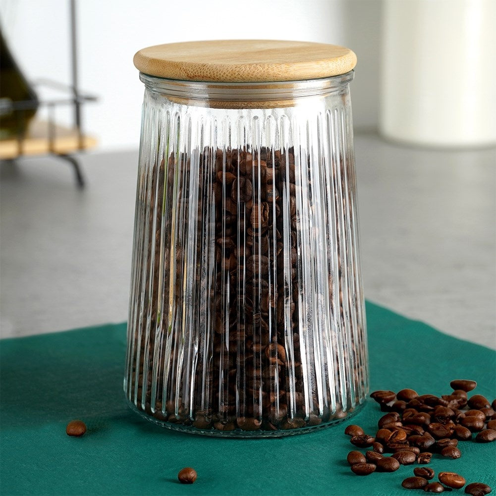Barattolo di vetro con coperchio in legno, riempito di chicchi di caffè, con chicchi sparsi.