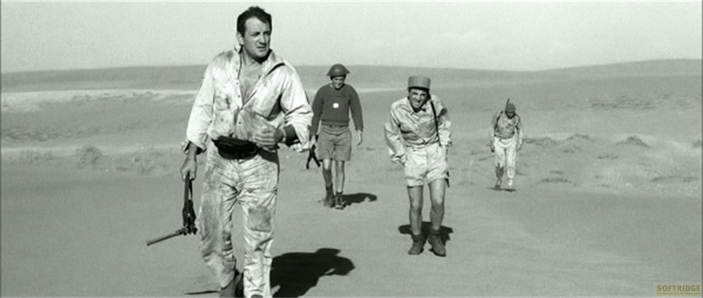 Quattro uomini in uniforme camminano in un paesaggio desertico sabbioso.
